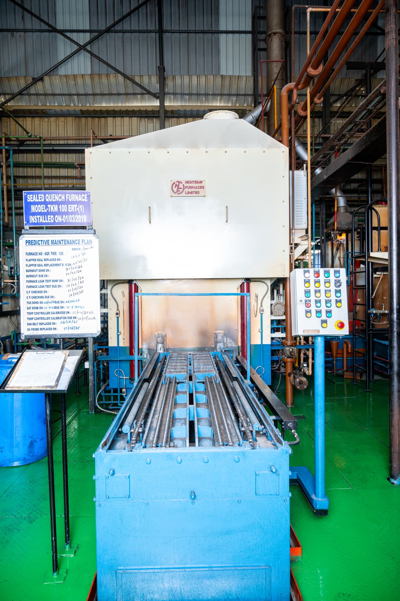 Sealed quench furnace on a heat treatment shop floor, with its control station and maintenance board alongside